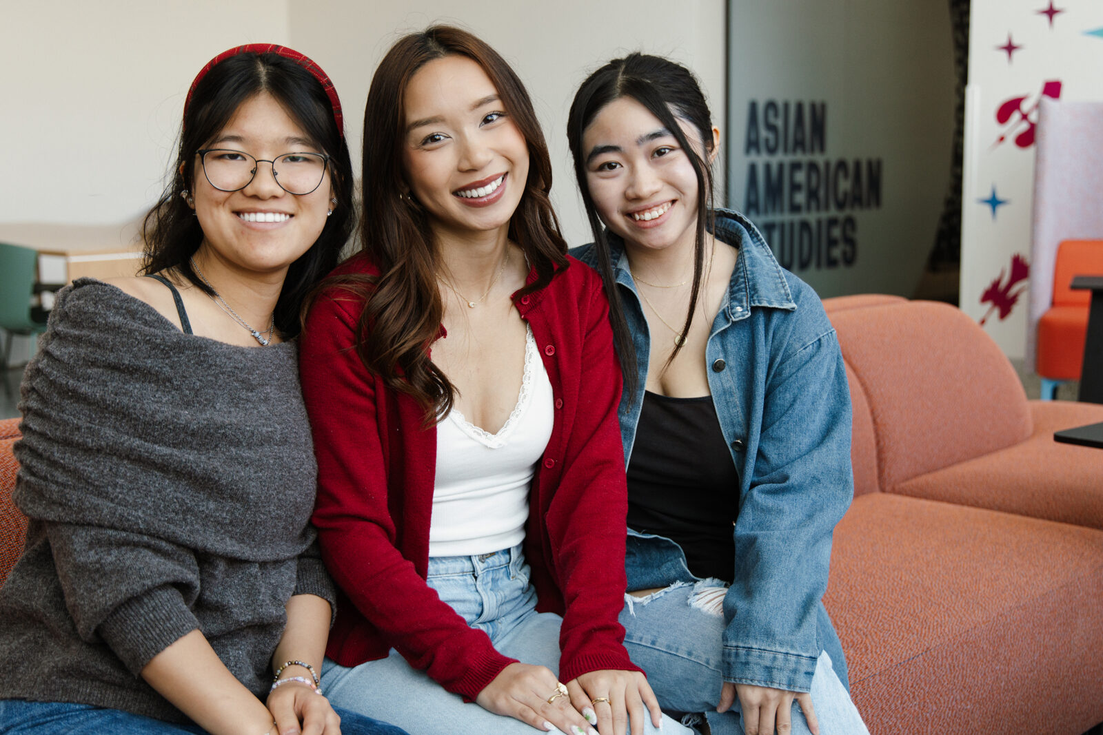Three student ambassadors smile to camera with the Asian American Studies home space behind them. 